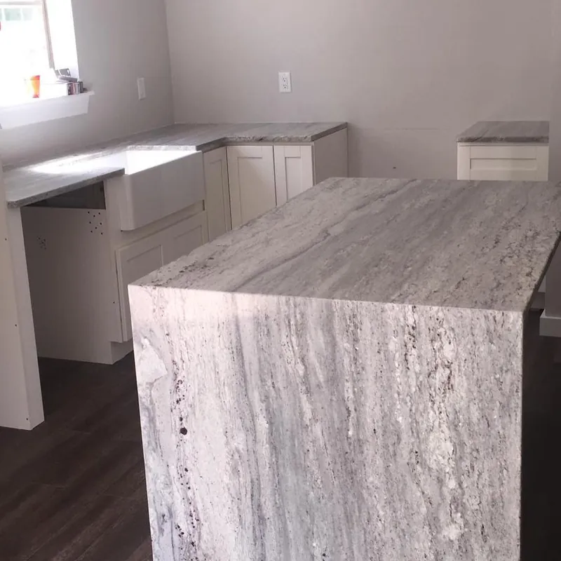 Island in linear gray-veined stone with a waterfall end, farmhouse sink beyond