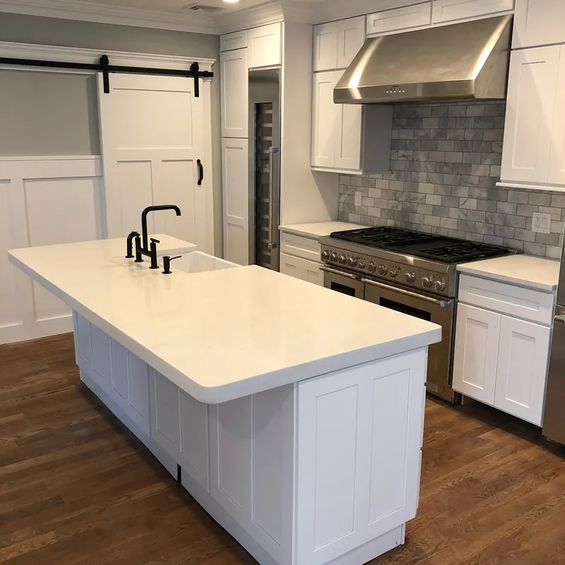 White quartz island with a black bridge faucet and farmhouse sink, professional range behind, Osterville, MA
