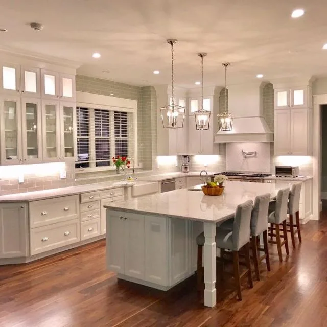 White Cape Cod kitchen with a light quartz island, lantern pendants and dark wood floor — installed by Cape Granite Connection